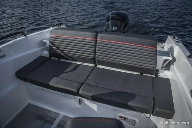 A sleek boat interior featuring a spacious black cushioned bench seat with red accents, overlooking a calm water surface.